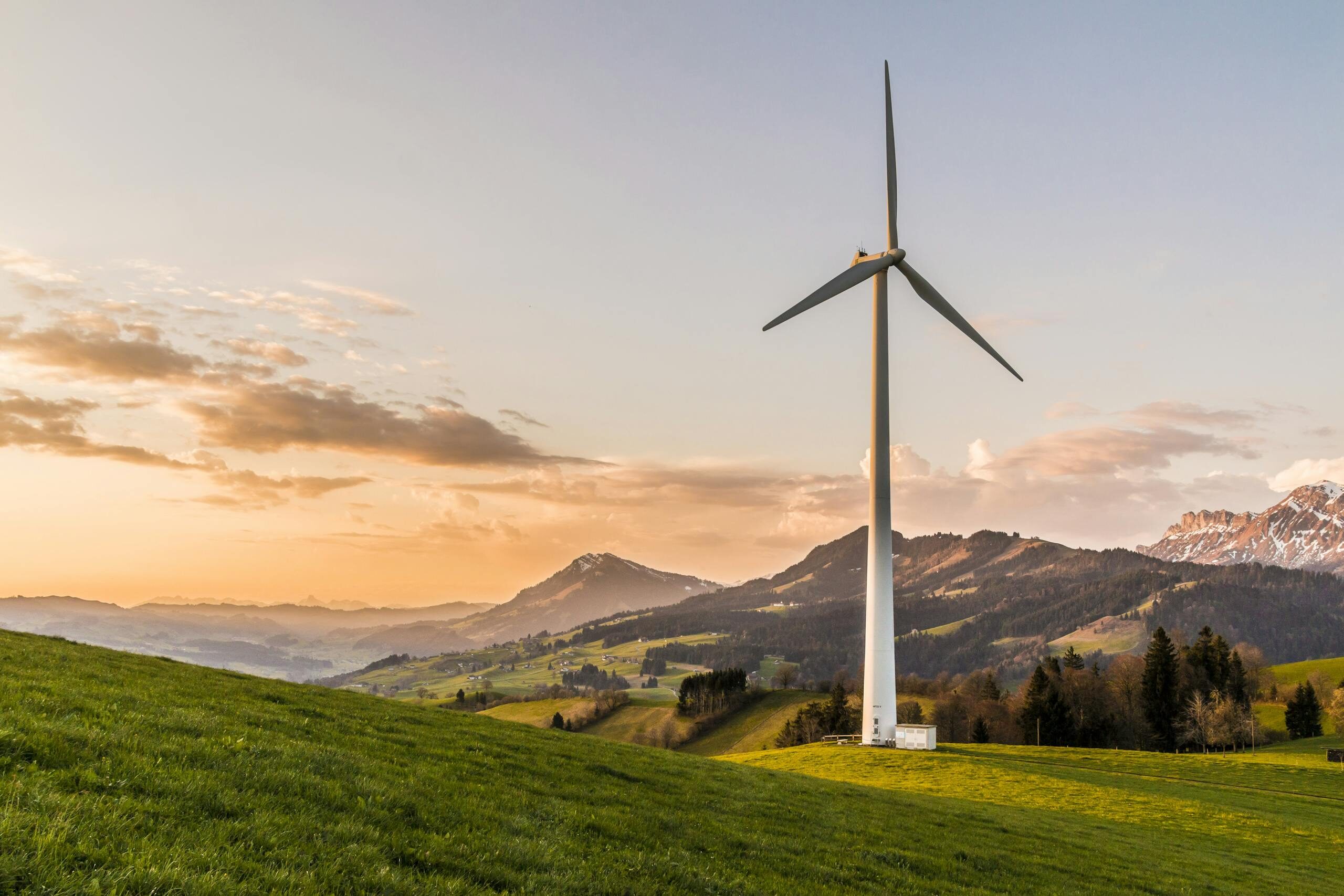 Wind turbine amid rolling hills and mountains at sunset, symbolizing renewable energy and sustainability.
