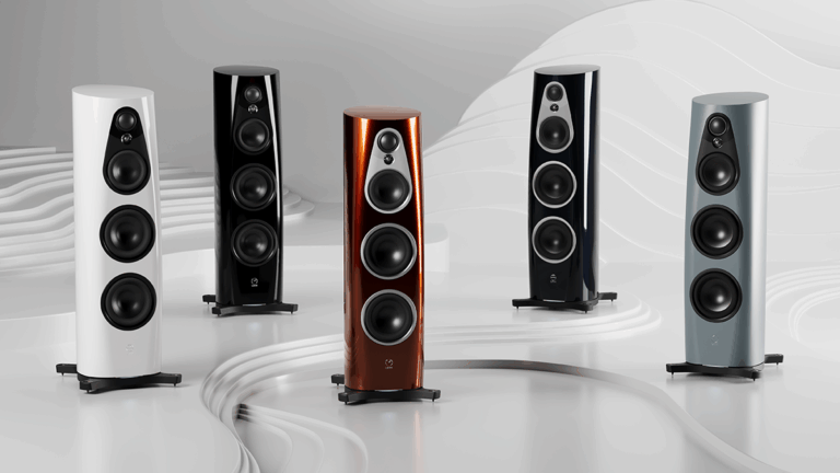 Five modern floorstanding hi-fi speakers in white, black, copper, dark blue, and light grey finishes arranged in a curved line on a glossy white surface with a sculpted, wave-like background.