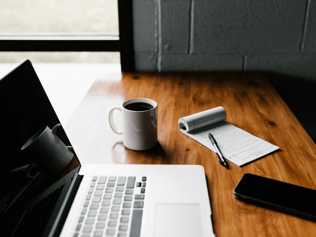 Workspace with laptop, notebook, and coffee on a desk, representing organised business operations, documentation, and day-to-day governance work at Xi Engineering Consultants.