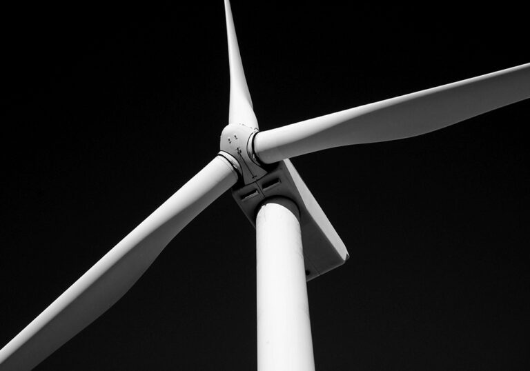 Black and white low-angle view of a wind turbine tower and three-bladed rotor against a dark sky.